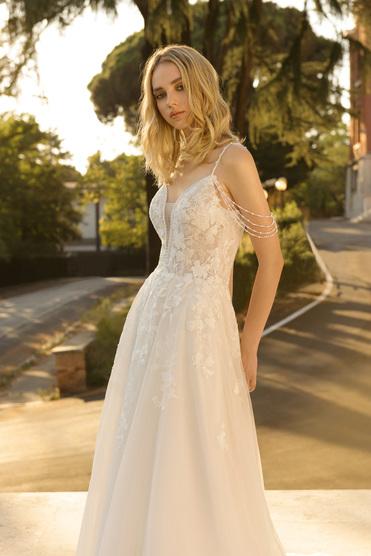 Eine junge Frau trägt ein fein besticktes Brautkleid, stehend im goldenen Licht der untergehenden Sonne, umgeben von grünen Bäumen.