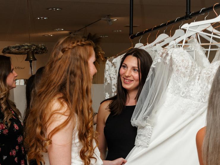 Brautberatung bei Clebeo Love Frau, die Brautkleid von Mitarbeiterin gezeigt bekommt im Brautladen